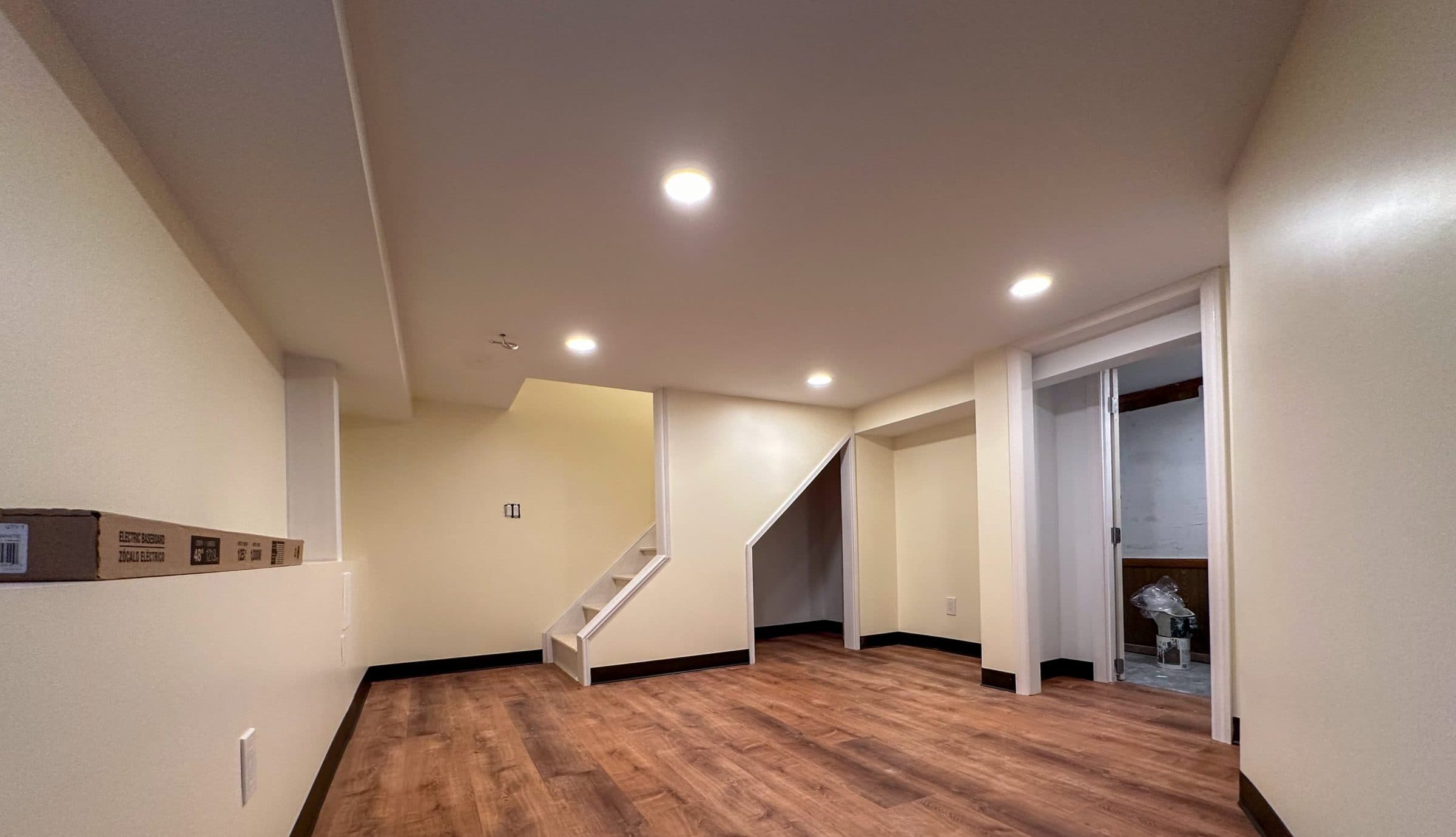 Finished basement with wood-look flooring, recessed lights and a white staircase