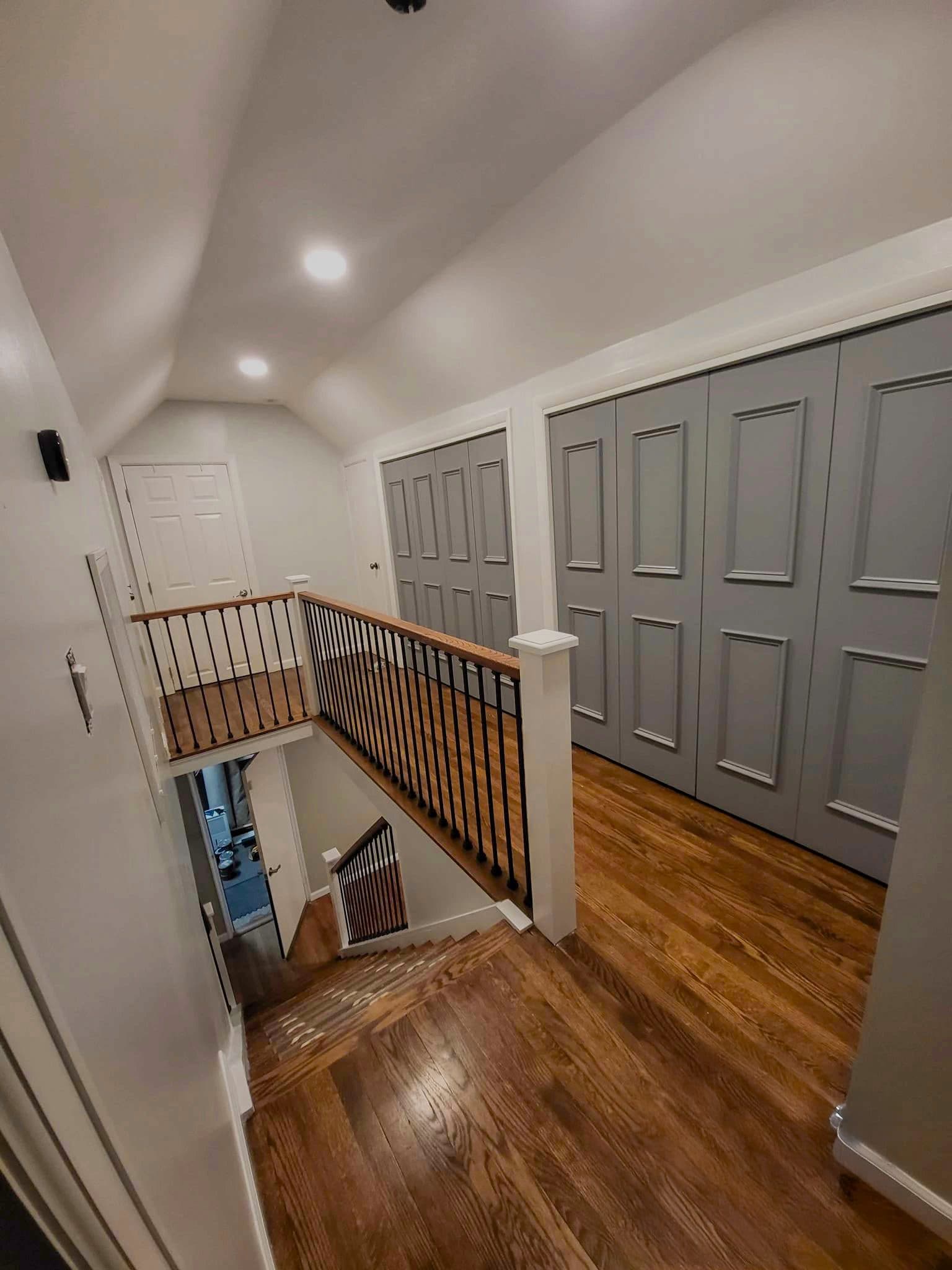 Upstairs hallway with hardwood floors, a stair railing with black balusters and gray closet doors